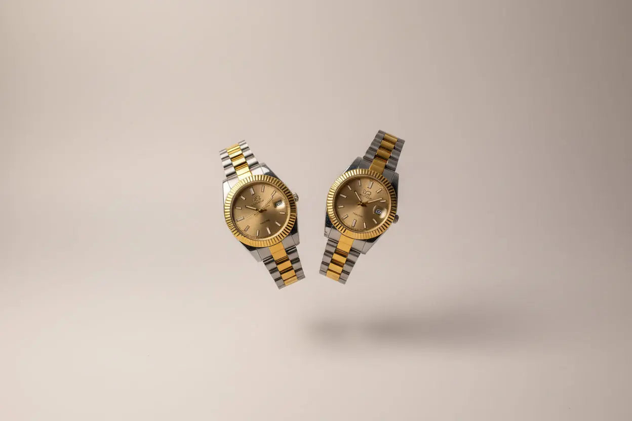 Two gold and silver watches on a person's wrist with a blurred indoor background.